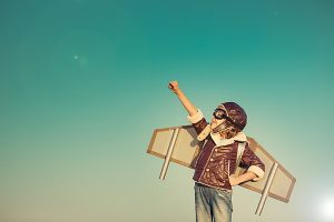 Kid pilot with toy jet pack against autumn sky background. Happy child playing outdoors
